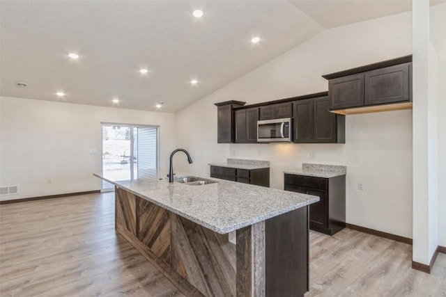 kitchen with stainless steel microwave, light stone counters, dark brown cabinetry, and a sink