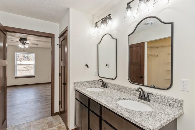 bathroom featuring a textured ceiling, double vanity, baseboards, and a sink