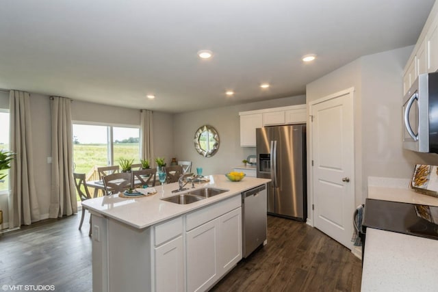 kitchen featuring dark wood-style floors, a center island with sink, a sink, appliances with stainless steel finishes, and white cabinetry
