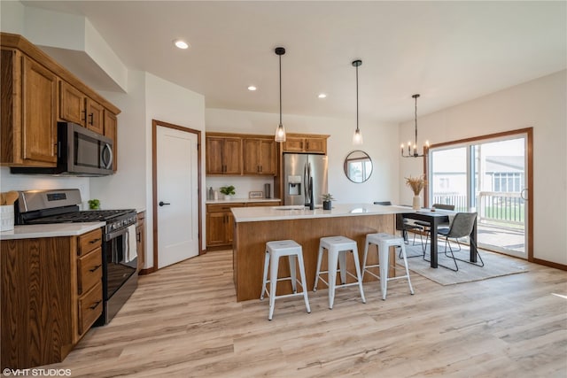 kitchen featuring an island with sink, stainless steel appliances, decorative light fixtures, light wood-type flooring, and an inviting chandelier