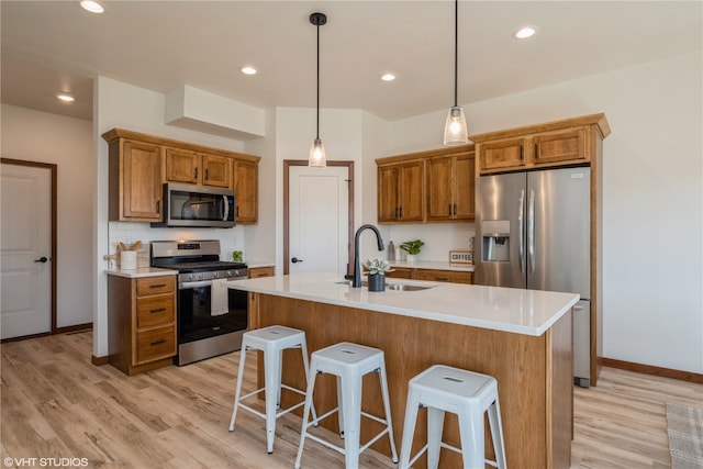 kitchen featuring an island with sink, pendant lighting, light hardwood / wood-style flooring, appliances with stainless steel finishes, and sink