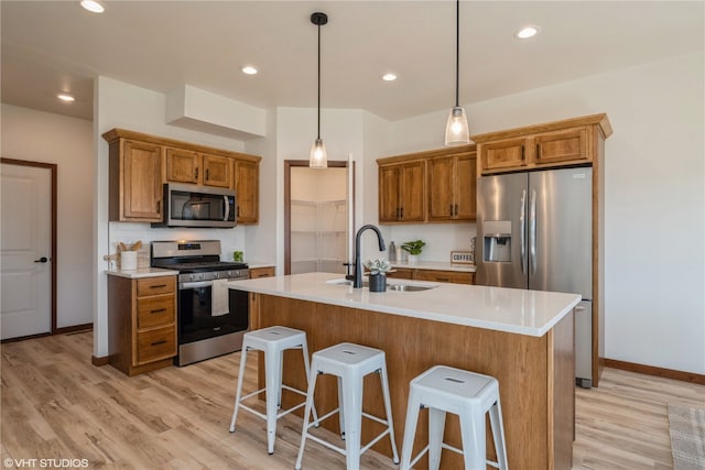 kitchen featuring appliances with stainless steel finishes, sink, an island with sink, light wood-type flooring, and pendant lighting