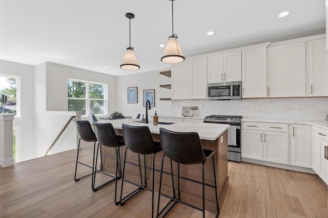 kitchen with light wood-type flooring, stainless steel appliances, plenty of natural light, and a kitchen island with sink