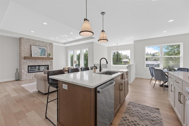 kitchen featuring a stone fireplace, decorative light fixtures, a kitchen island with sink, light hardwood / wood-style floors, and dishwasher