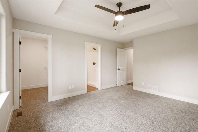 unfurnished bedroom with a raised ceiling, carpet, a spacious closet, and ensuite bath