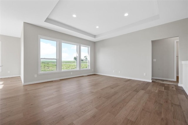 interior space with light wood-type flooring, baseboards, a tray ceiling, and recessed lighting