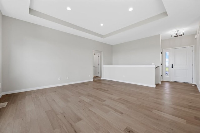 unfurnished room with a tray ceiling, light wood-style flooring, baseboards, and recessed lighting