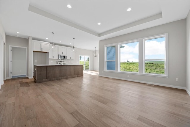 unfurnished living room with a raised ceiling, light wood-style flooring, and baseboards