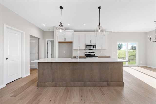 kitchen with a sink, white cabinetry, light countertops, appliances with stainless steel finishes, and a large island with sink