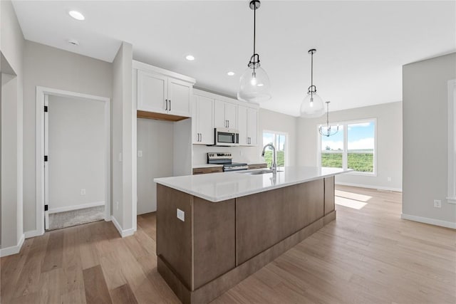 kitchen featuring light wood-style flooring, stainless steel appliances, light countertops, white cabinetry, and a sink