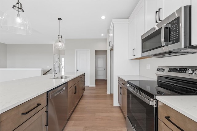 kitchen with light wood finished floors, white cabinets, hanging light fixtures, stainless steel appliances, and a sink