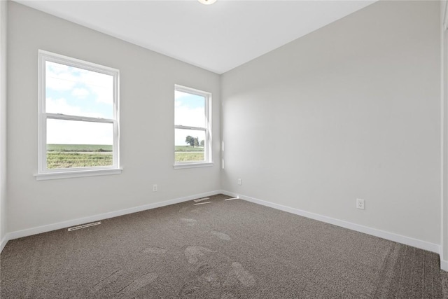 empty room with dark colored carpet, visible vents, and baseboards