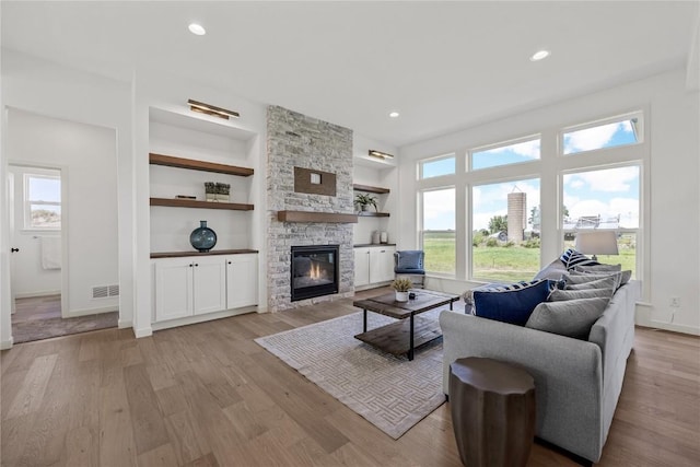 living room with light wood-type flooring, built in shelves, a fireplace, and visible vents