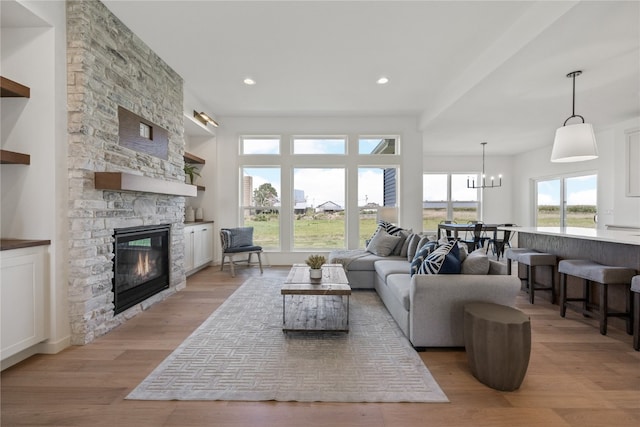 living room featuring light hardwood / wood-style floors, a chandelier, and a stone fireplace