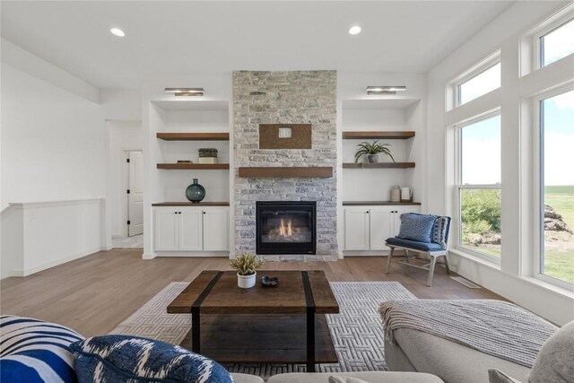 living room with light hardwood / wood-style floors, a stone fireplace, and built in features