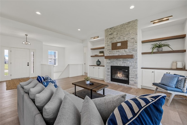 living room with built in features, light hardwood / wood-style floors, and a stone fireplace