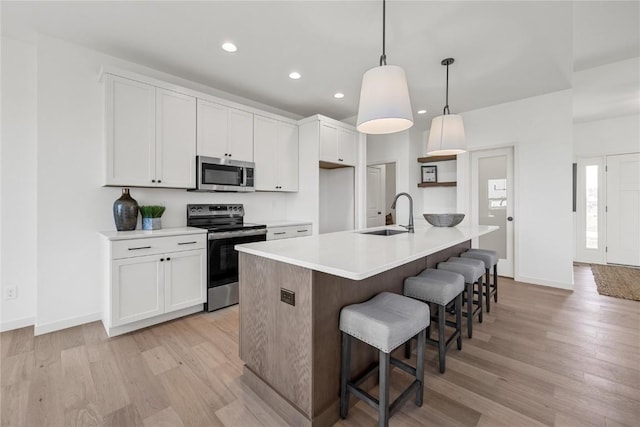 kitchen with white cabinets, an island with sink, appliances with stainless steel finishes, light countertops, and a sink