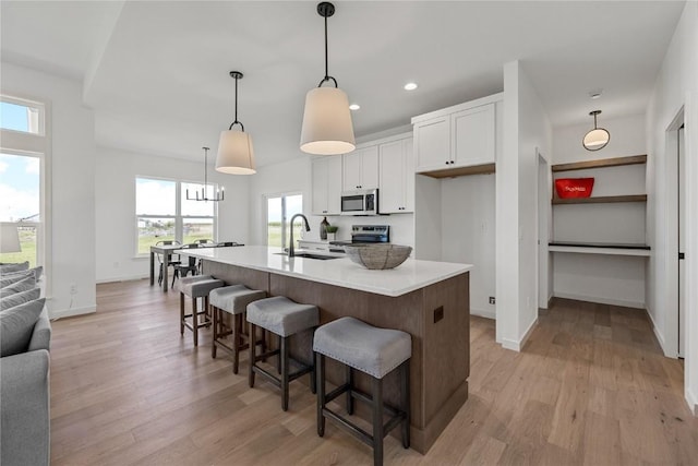 kitchen featuring pendant lighting, appliances with stainless steel finishes, white cabinets, a sink, and an island with sink