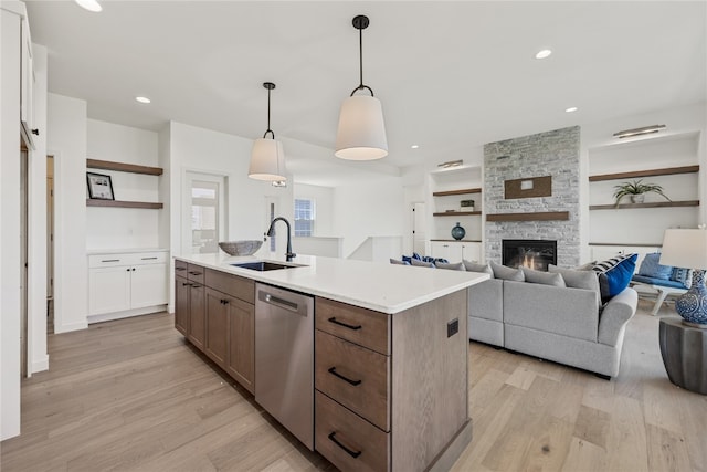 kitchen featuring sink, a fireplace, an island with sink, light hardwood / wood-style floors, and stainless steel dishwasher