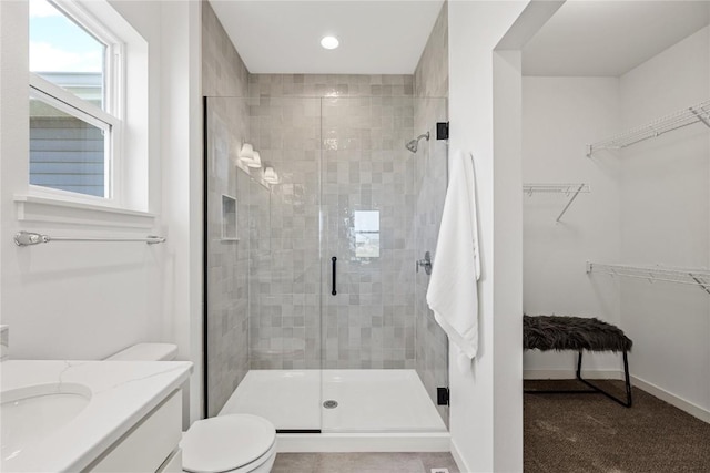 full bath with a spacious closet, toilet, a shower stall, vanity, and baseboards