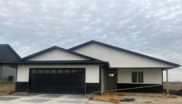 view of front of property featuring stone siding, central AC, an attached garage, and concrete driveway