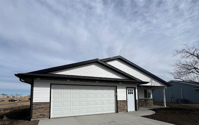 view of front of home featuring a garage, stone siding, central AC, and driveway