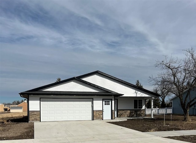 view of front of house with driveway, stone siding, an attached garage, and fence