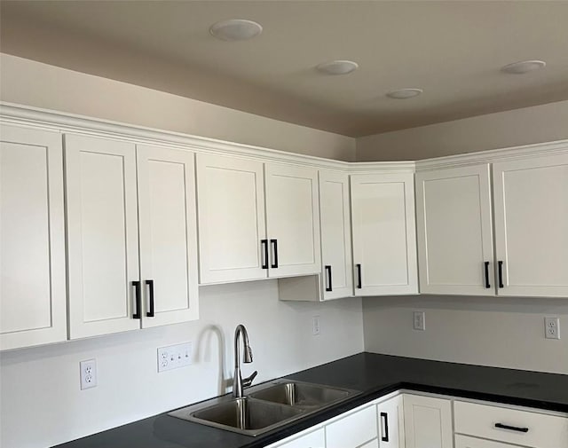 kitchen featuring dark countertops, white cabinets, and a sink