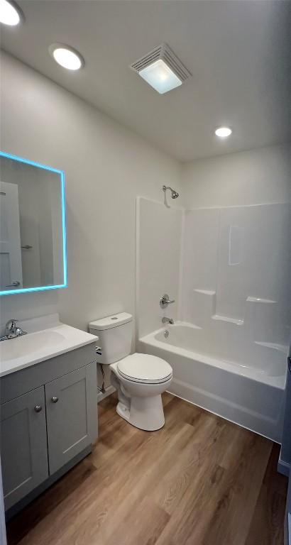 bathroom featuring toilet, wood finished floors, vanity, visible vents, and tub / shower combination