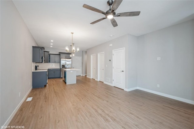 unfurnished living room featuring ceiling fan with notable chandelier and light wood-type flooring