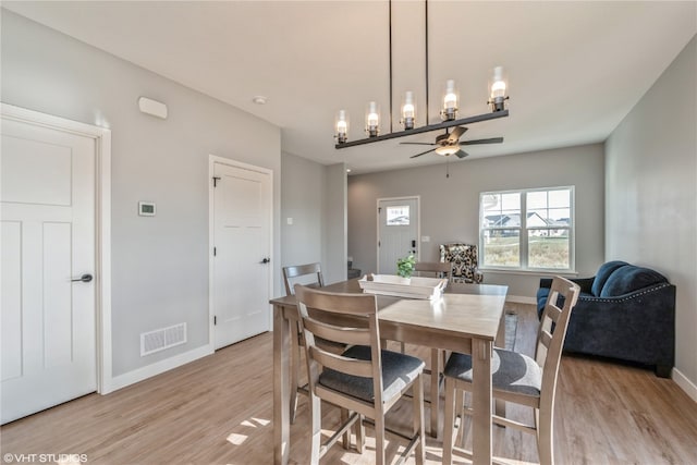 dining room with light hardwood / wood-style flooring and ceiling fan with notable chandelier