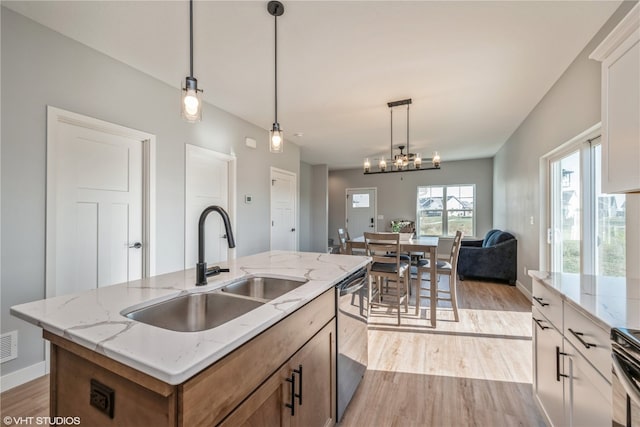 kitchen with sink, an island with sink, dishwasher, light hardwood / wood-style floors, and pendant lighting