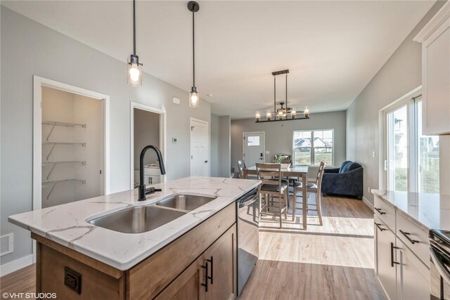 kitchen featuring light wood-type flooring, sink, an island with sink, and white cabinets