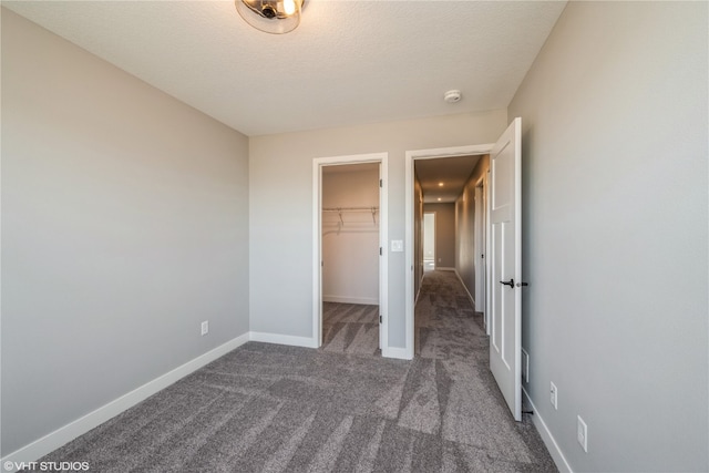 unfurnished bedroom featuring a closet, a textured ceiling, a spacious closet, and dark colored carpet