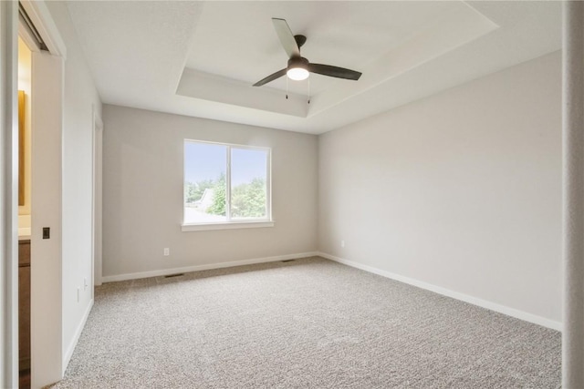 carpeted empty room featuring a raised ceiling and ceiling fan