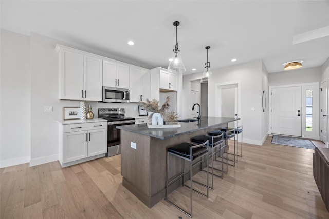 kitchen featuring white cabinets, a center island with sink, appliances with stainless steel finishes, light hardwood / wood-style floors, and sink