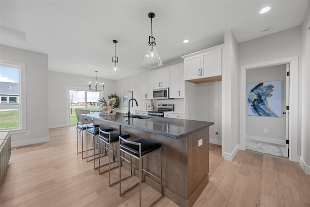 kitchen featuring a large island with sink, appliances with stainless steel finishes, white cabinetry, and light hardwood / wood-style floors