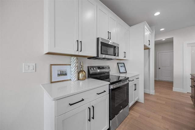 kitchen with appliances with stainless steel finishes, light hardwood / wood-style flooring, and white cabinets