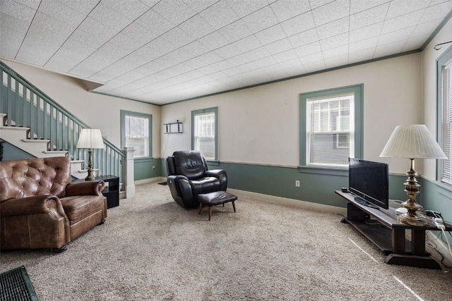 carpeted living area with stairs, crown molding, and baseboards