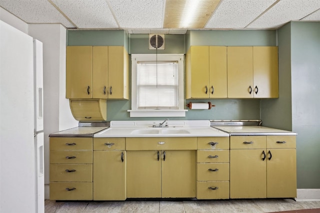 kitchen featuring visible vents, light countertops, freestanding refrigerator, a paneled ceiling, and a sink