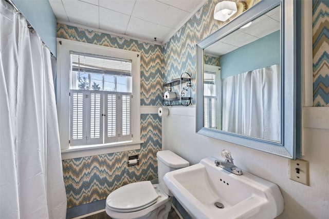 full bath featuring toilet, wallpapered walls, and a sink