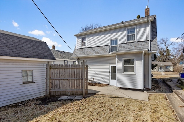 rear view of property featuring roof with shingles, a chimney, and fence