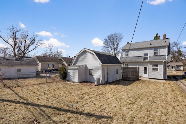 back of property with a gambrel roof, fence, a shed, an outdoor structure, and a shingled roof