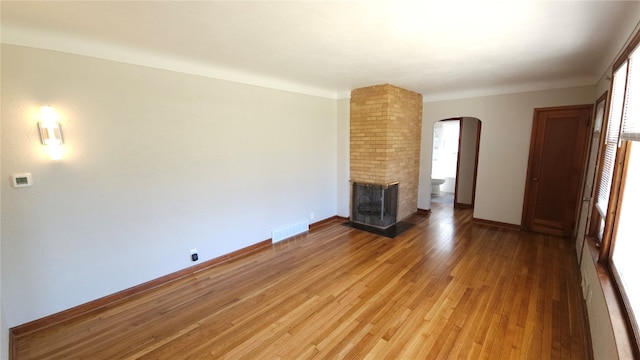 unfurnished living room featuring wood-type flooring, brick wall, and a brick fireplace