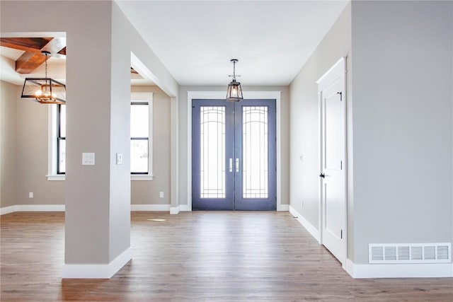 entrance foyer with french doors, coffered ceiling, beamed ceiling, a chandelier, and light wood-type flooring