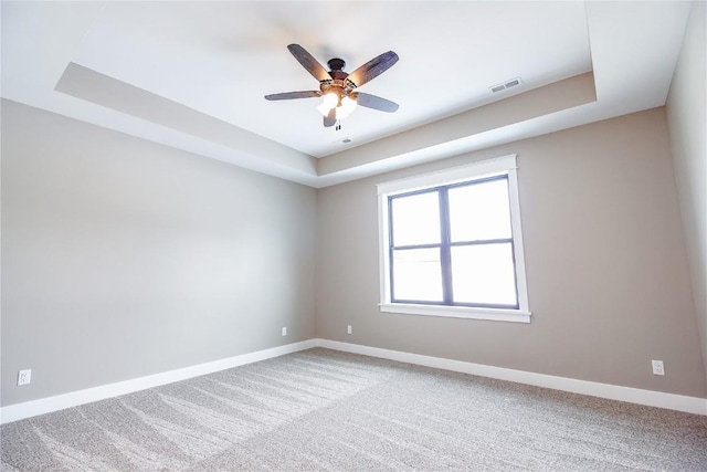 carpeted spare room featuring ceiling fan and a raised ceiling