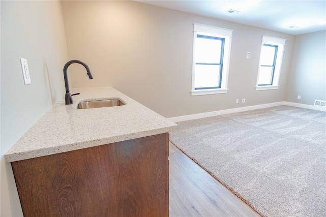 kitchen featuring light wood-type flooring, light stone counters, and sink