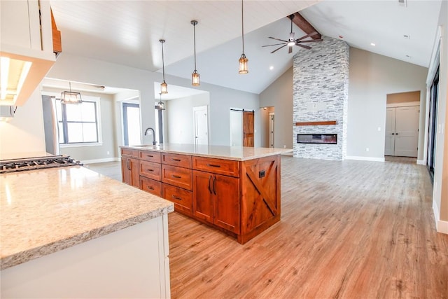 kitchen with a stone fireplace, sink, hanging light fixtures, ceiling fan, and beamed ceiling