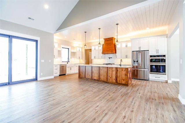 kitchen with appliances with stainless steel finishes, premium range hood, a spacious island, pendant lighting, and white cabinets