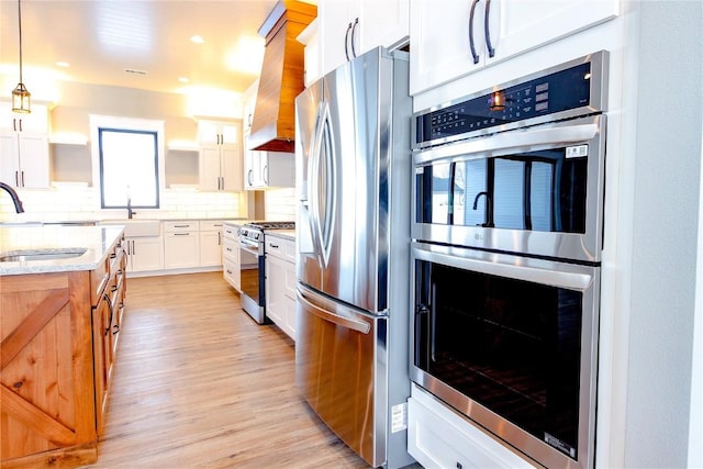 kitchen with appliances with stainless steel finishes, custom exhaust hood, sink, decorative light fixtures, and white cabinetry